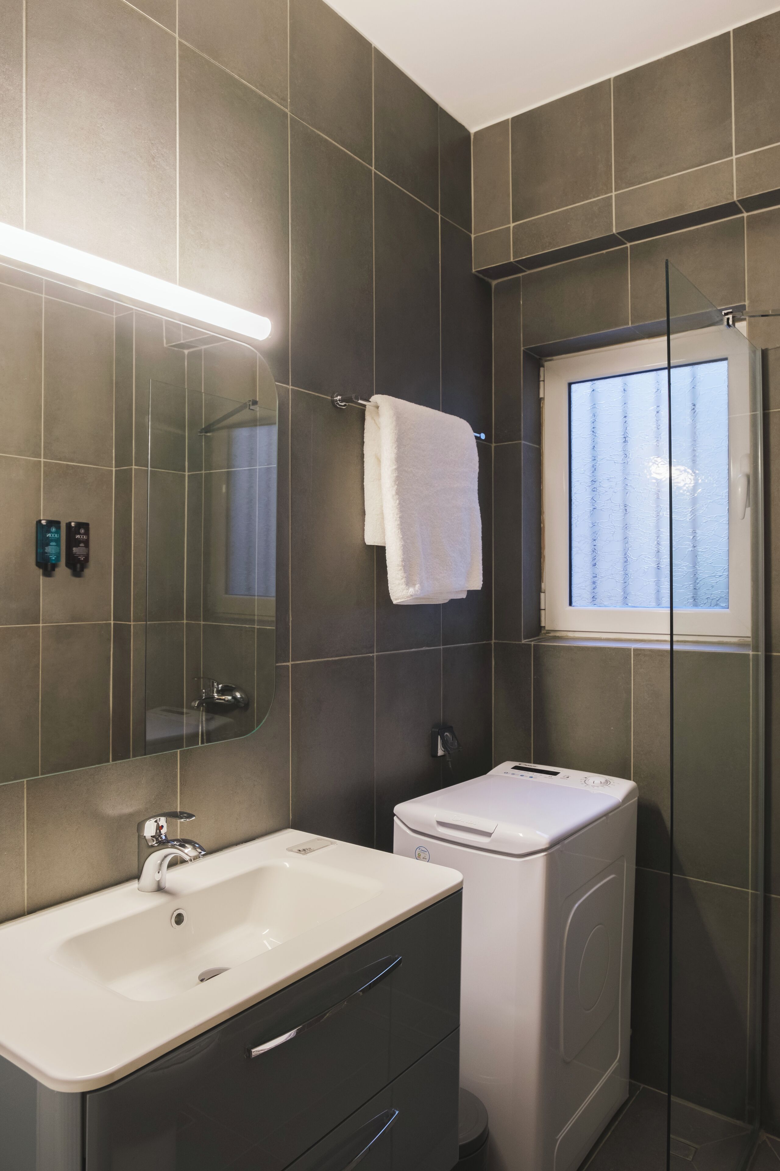 Une salle de bain moderne avec un grand miroir, un lavabo, une douche et une fenêtre.