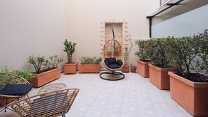 Un espace patio aménagé avec des meubles en osier, des plantes en pot et un fauteuil suspendu.