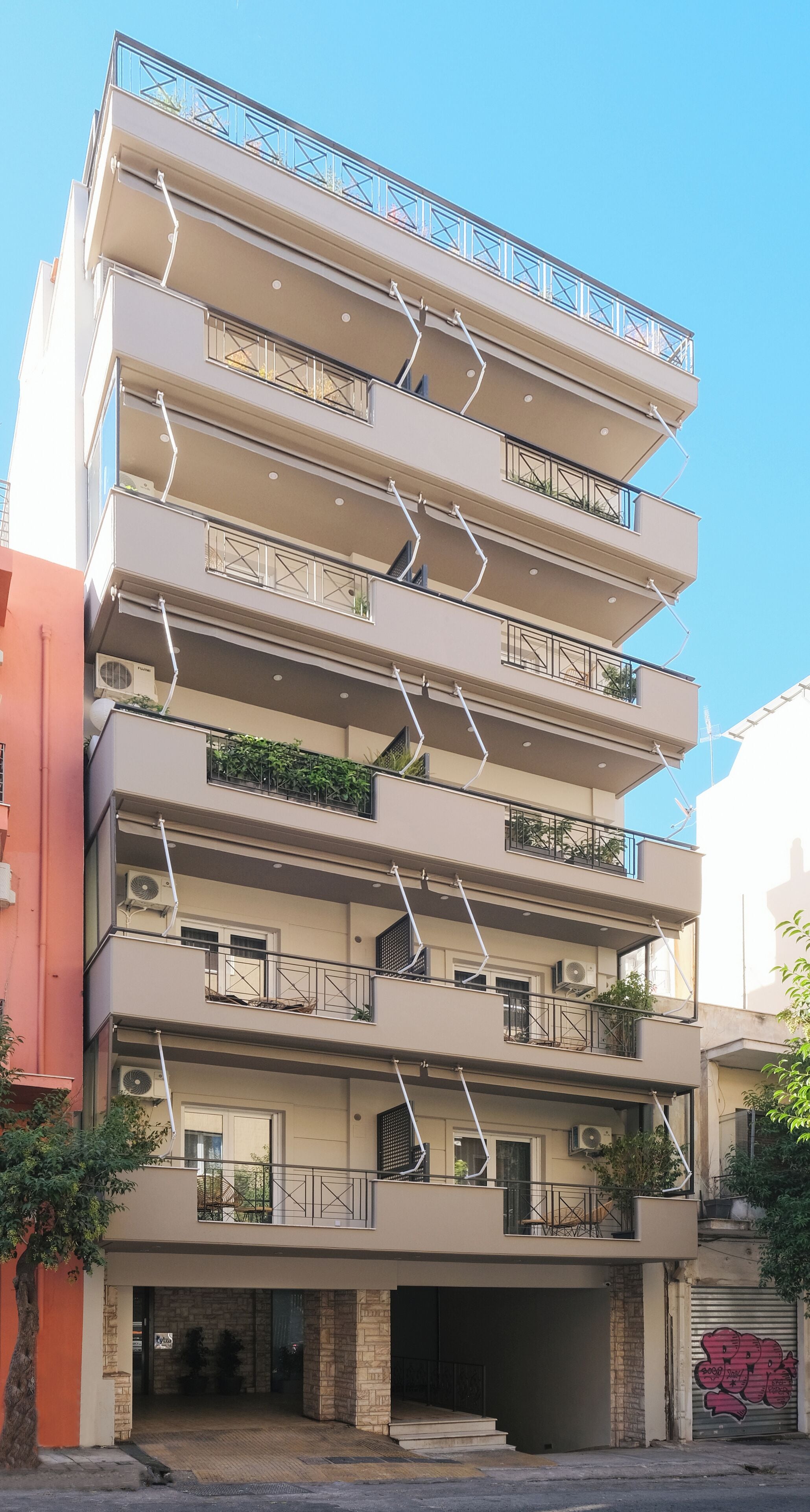 Un edificio residencial de varios pisos con balcones, unidades de aire acondicionado y la entrada de un garaje.
