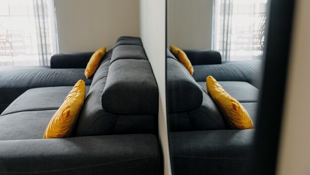A modern living room with a sofa and a large mirror reflecting the room.