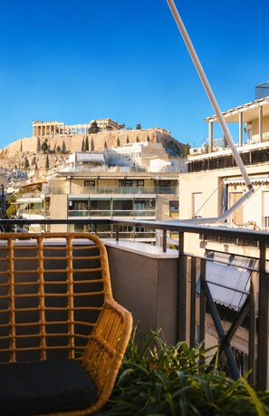 A balcony with wicker furniture, a view of modern buildings, and ancient ruins in the background. - Tyto Alba Habitat (Athens)