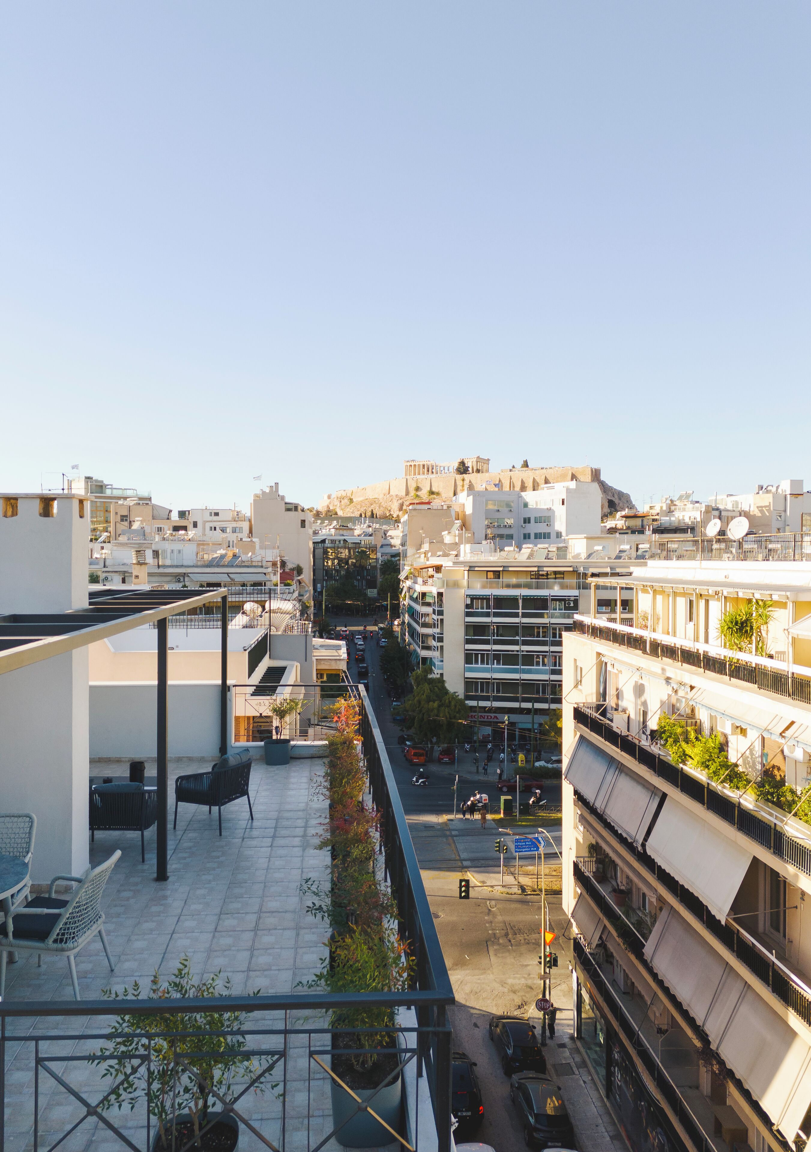 A rooftop terrace with outdoor seating, a view of the cityscape, and a clear sky.