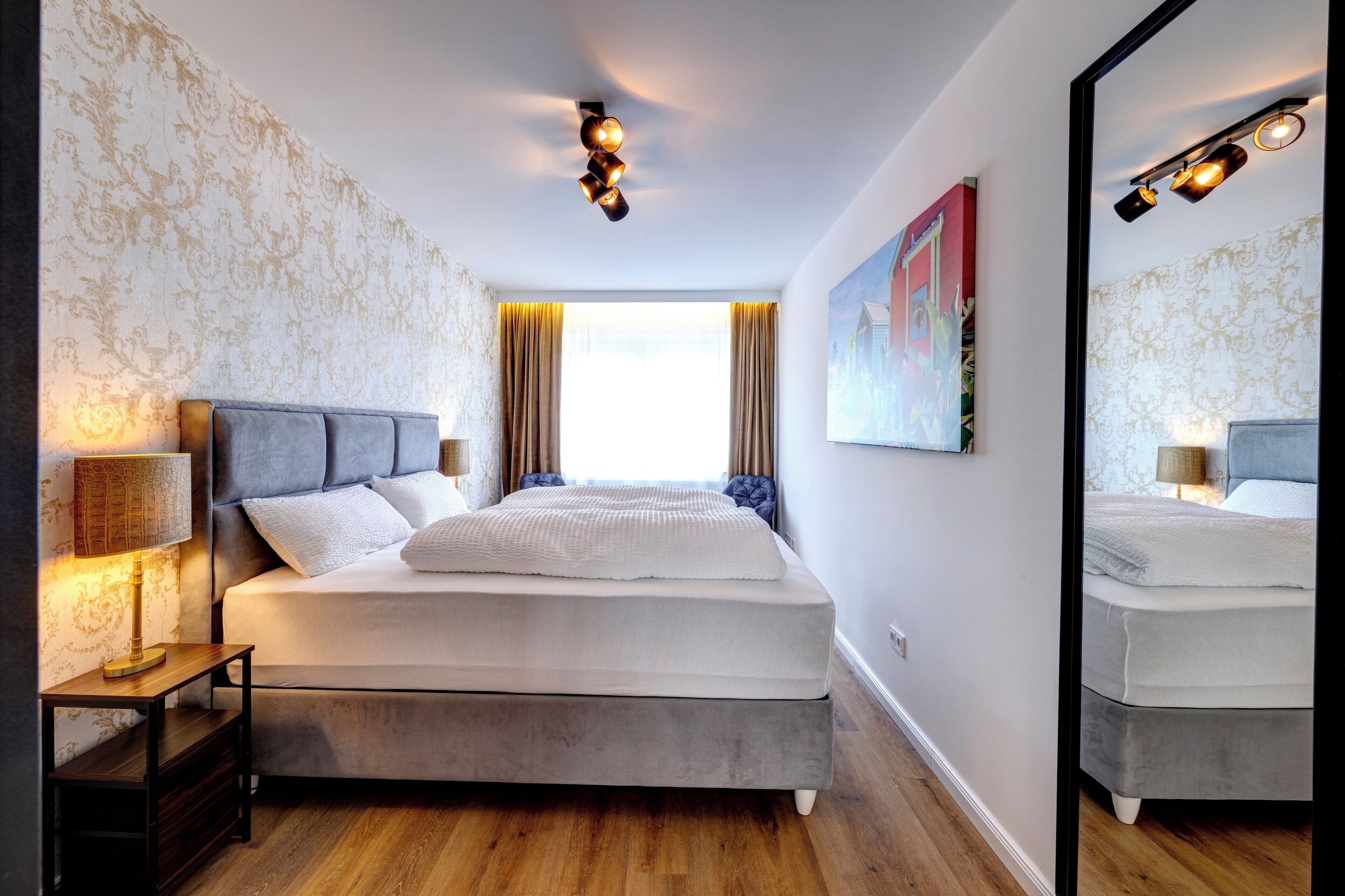 A modern bedroom with a large bed, a bedside table with a lamp, and a large mirror.