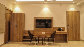 Ein modernes Zimmer mit Schreibtisch aus Holz, zwei Stühlen, einem Flachbildfernseher und einem Deckenventilator.