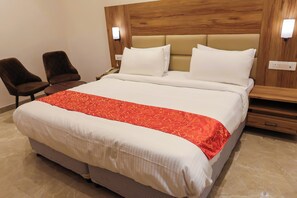 A hotel room with a large bed, two chairs, a wooden headboard, and a bedside table. - Hotel SS Grand (Kanpur)