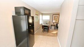 A compact kitchen with a black refrigerator, a microwave, and a dining area with a table and chairs. - 1 Bedroom Apartment Near Notre Dame 1309 5 (South Bend)