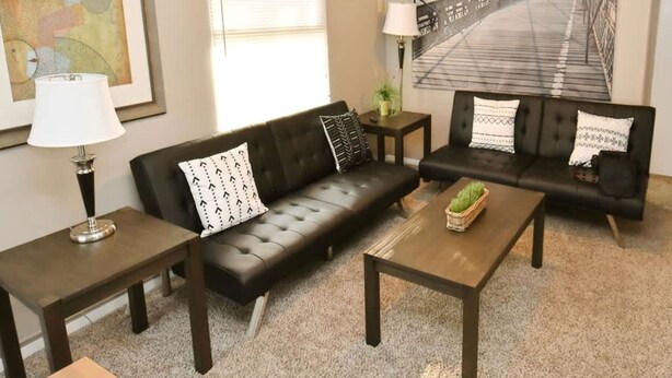 A living room with a sofa set, a coffee table, a lamp, and a painting of a bridge. - 1 Bedroom Apartment Near Notre Dame 1309 5 (South Bend)
