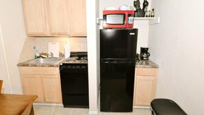 Una cocina compacta con armarios de madera, un refrigerador negro, un microondas y una estufa.