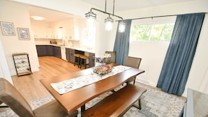 Uma sala de jantar com uma mesa de madeira, bancos e uma cozinha ao fundo.