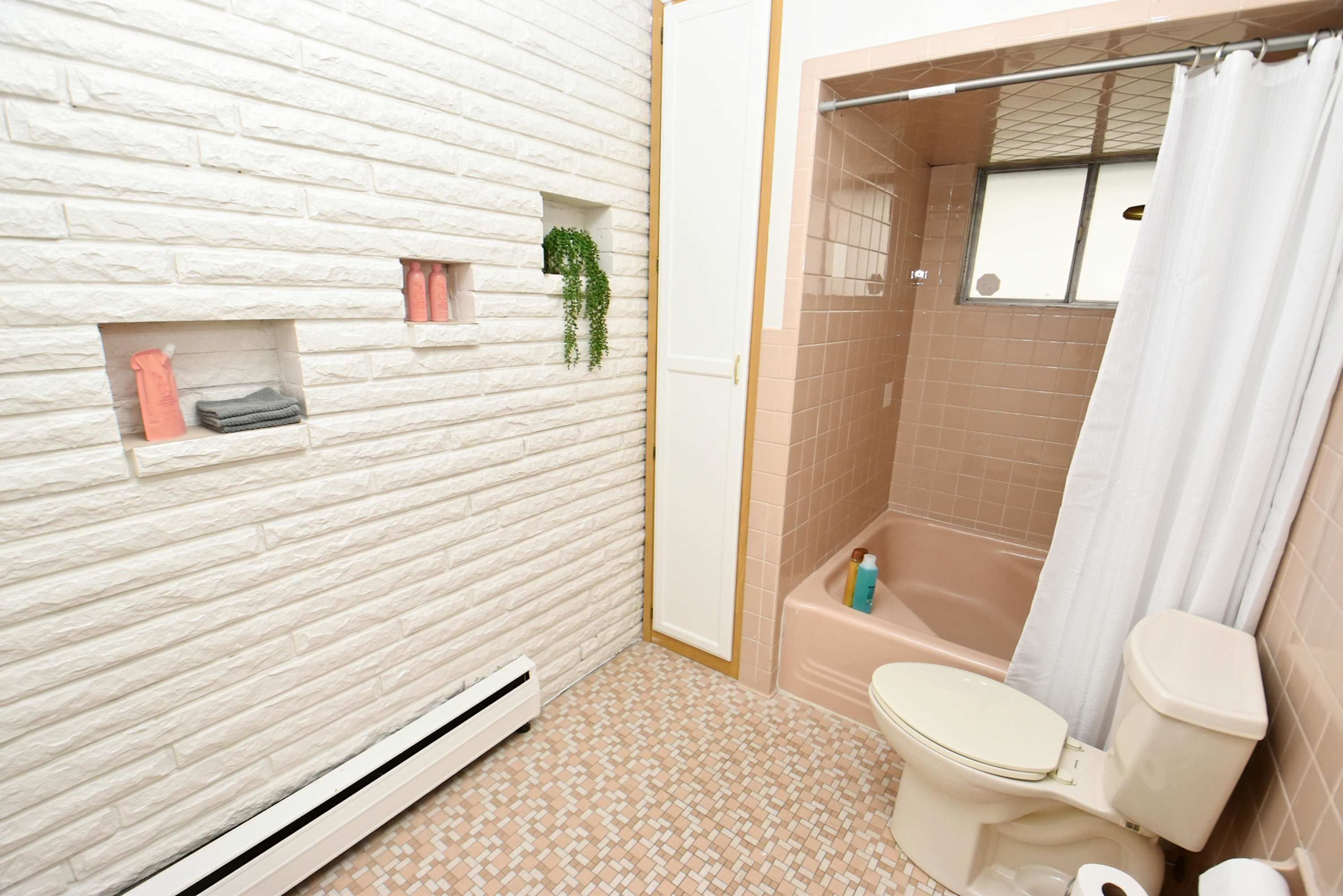 A bathroom with a white brick wall, a beige bathtub, a toilet, and a shower curtain.