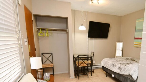 A compact bedroom with a bed, a small desk, a chair, a sofa, and a TV mounted on the wall.