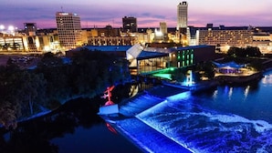 A waterfront hotel with a glass facade, a water feature, and a city skyline in the background.