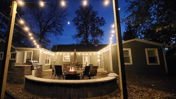 Eine Außenpatio-Terrasse mit Feuerstelle, Sitzgelegenheiten und Lichterketten.
