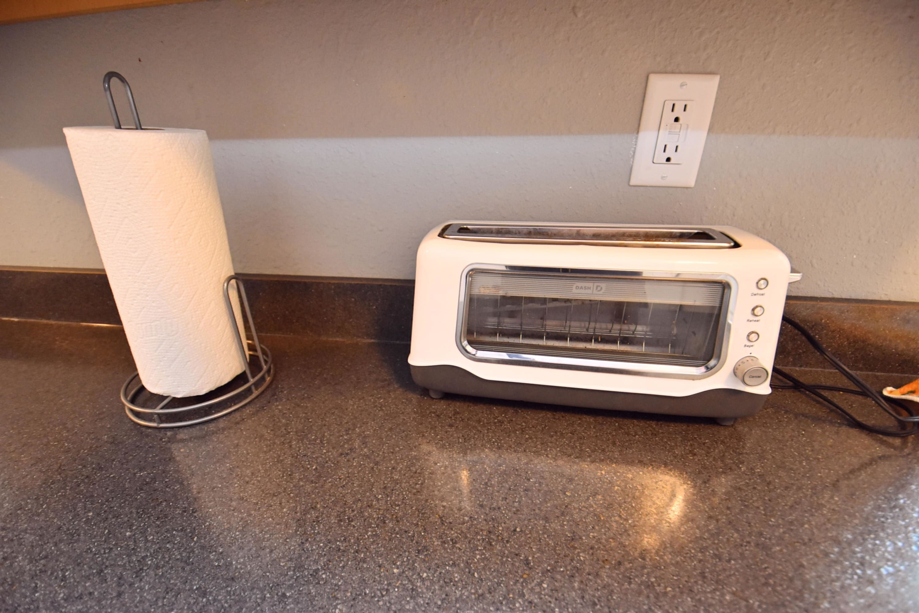 A kitchen with a toaster and a paper towel holder on a granite countertop.