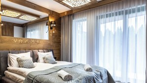 Un dormitorio moderno con una cama grande, cabecera de madera y vistas a un bosque a través de cortinas traslúcidas.