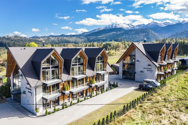 Une rangée d’immeubles modernes à plusieurs étages, dotés de grandes fenêtres et de balcons en bois, se dressant sur un fond de montagnes et d’un ciel dégagé.