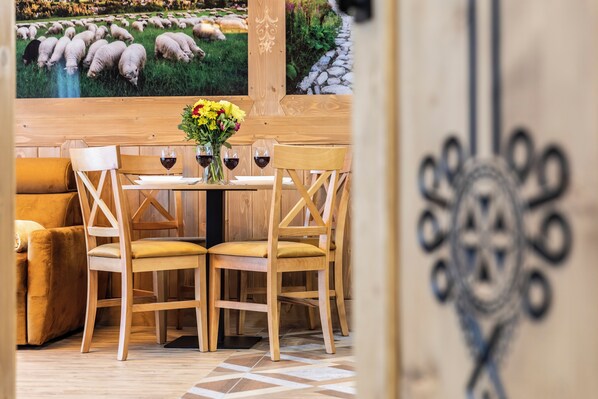 A dining area with a wooden table, four chairs, a vase of flowers, and two glasses of red wine.