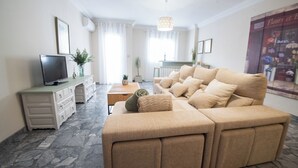 A living room with a beige sofa, a TV on a cabinet, and a plant on a side table. - Molino suites, apt Ronda, two bedrooms en suite in the center of the city  (Ronda)