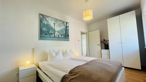 Une chambre à coucher comprenant un lit, des tables de chevet, un luminaire suspendu, une porte et une armoire.