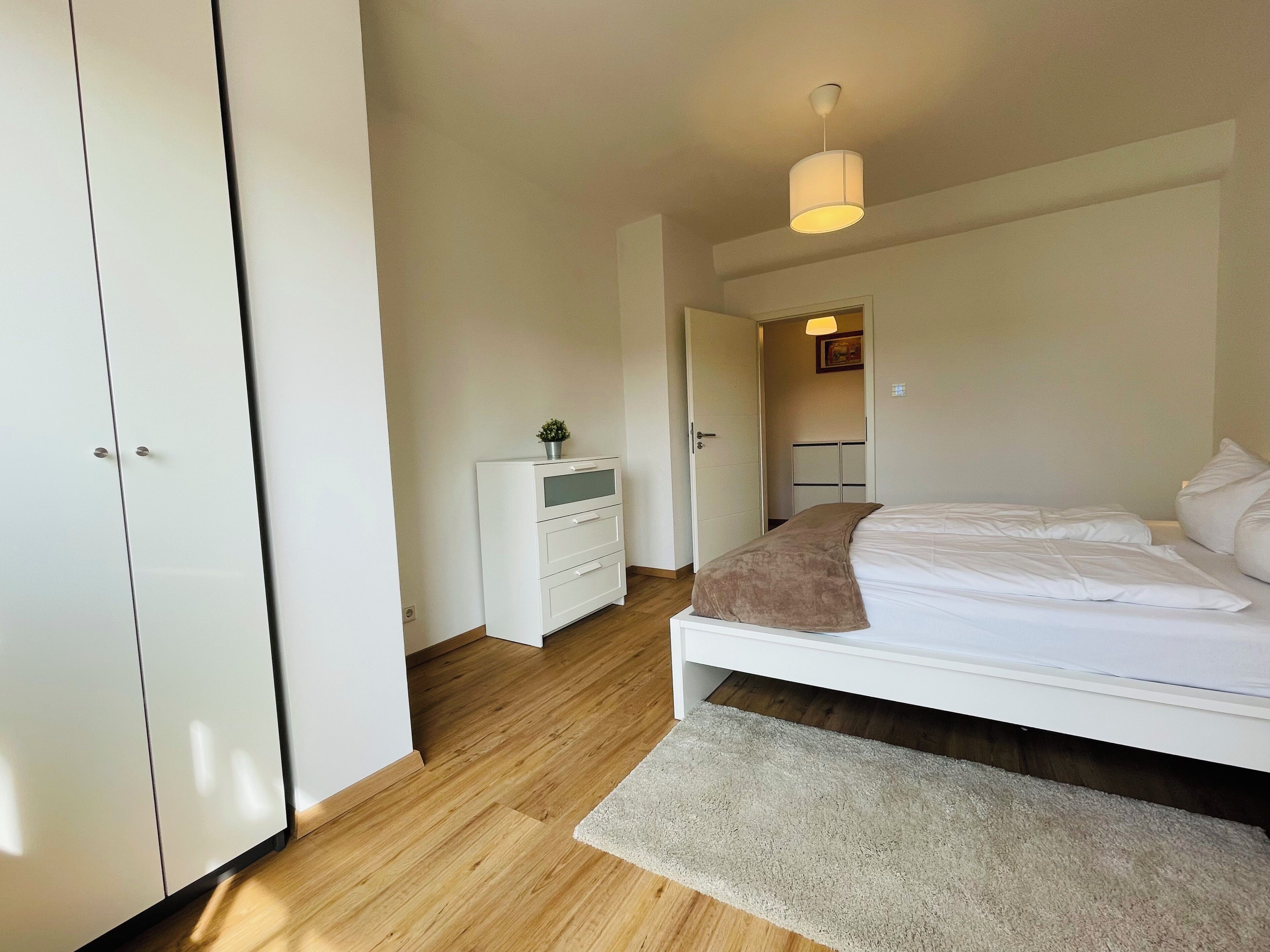 Une chambre à coucher comprenant un lit, une table de chevet, une armoire et une porte donnant sur une autre pièce.