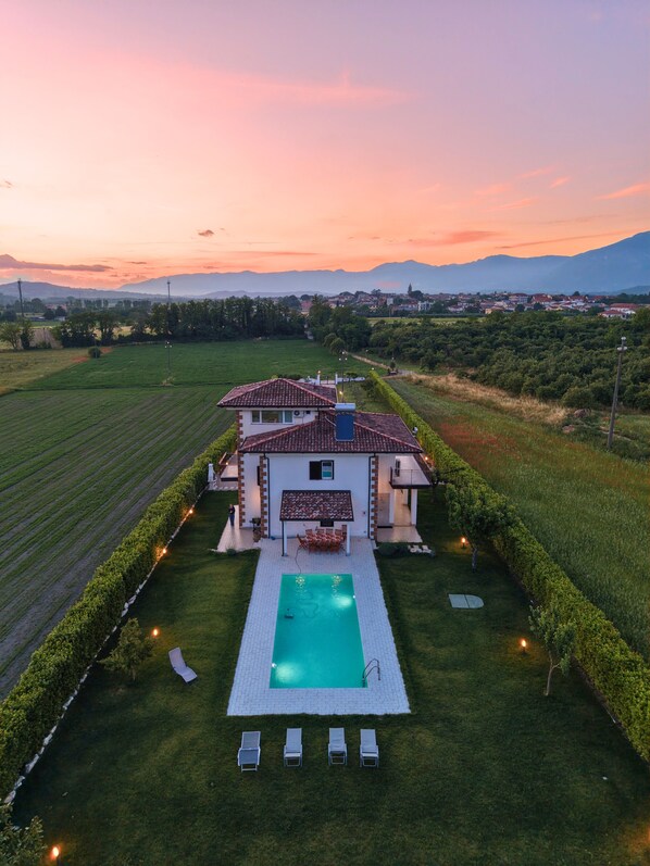 A villa with a swimming pool, surrounded by a well-maintained lawn and hedges.