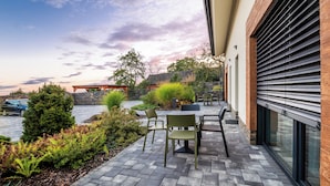 Un patio al aire libre con piso de ladrillo, una mesa con sillas y vista a un muro de piedra y árboles.