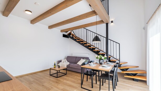 Una sala de estar moderna con una escalera de madera, un sofá, una mesa de comedor con sillas y una mesa baja.