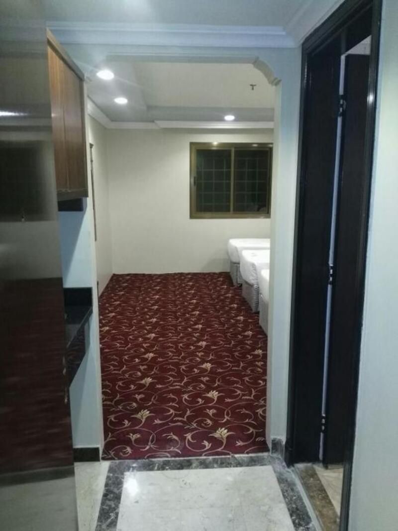 Un couloir étroit avec un tapis à motifs, une fenêtre à carreaux et une salle de bain blanche équipée de toilettes et d’un lavabo.