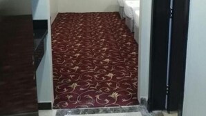 A narrow hallway with a patterned carpet, a window with a grid pattern, and a white bathroom with a toilet and sink. - Sama AlMisk Hotel (Makkah)