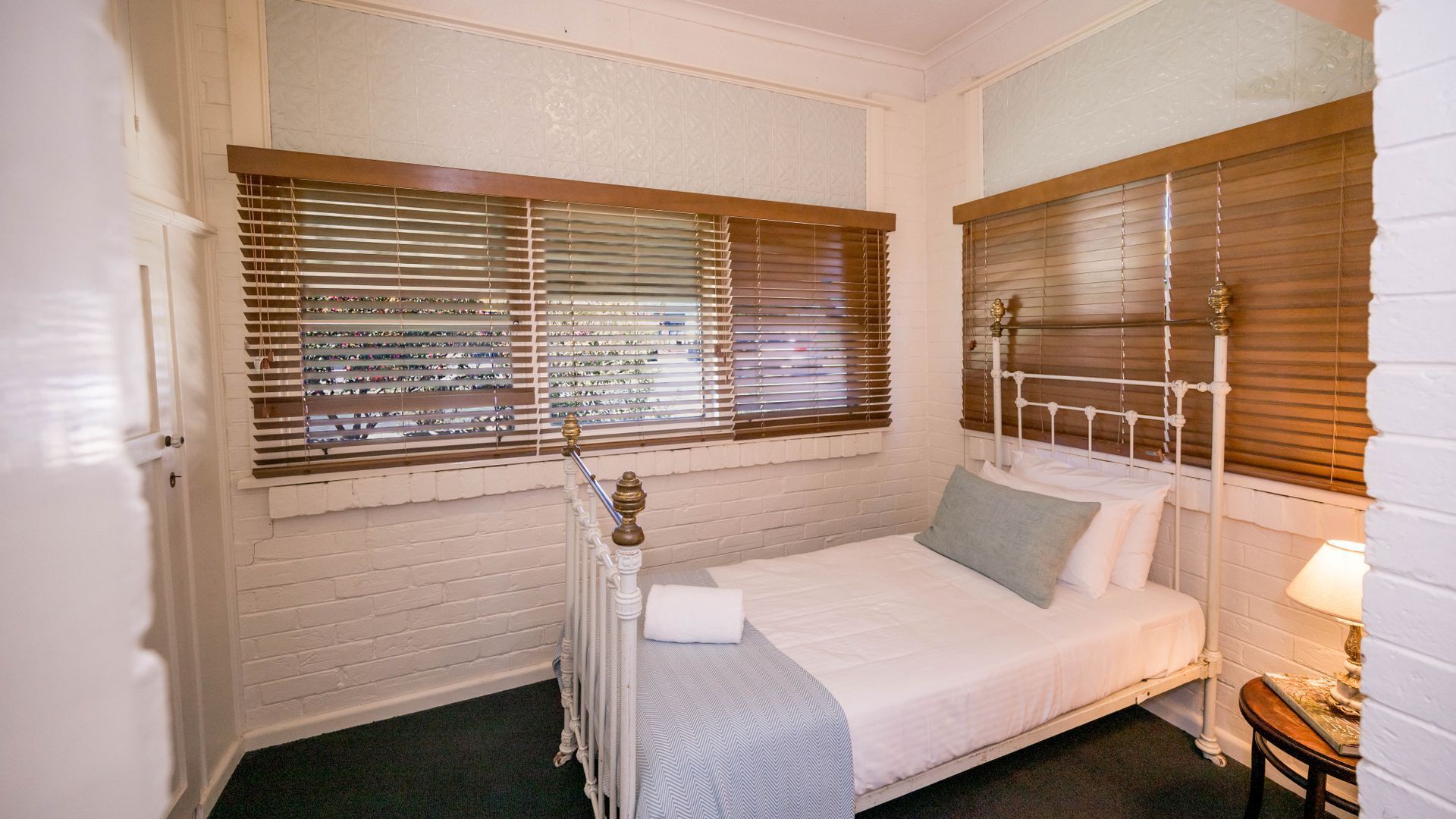 Een knus slaapkamer met een enkel bed, een nachtkastje en een raam met zonwering.