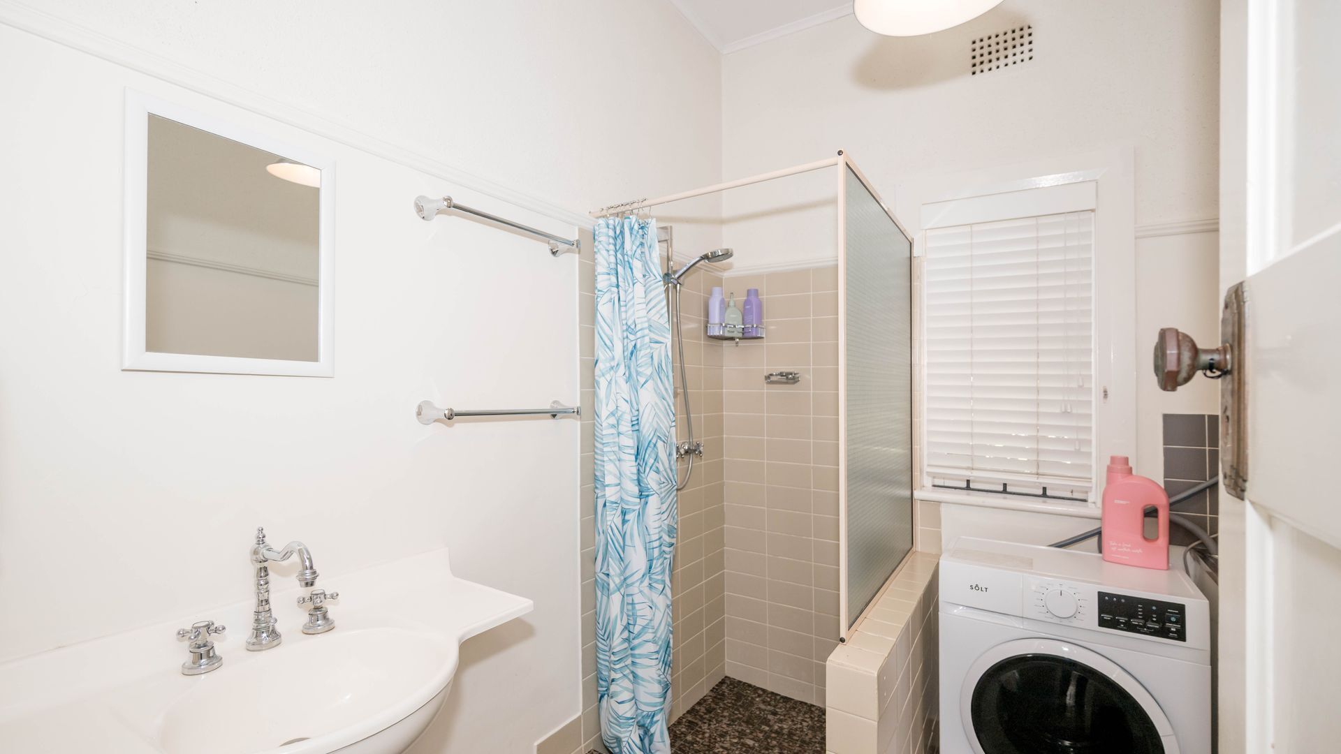 Une petite salle de bain comprenant un lavabo, une douche avec un rideau de douche bleu, un miroir et un lave-linge.