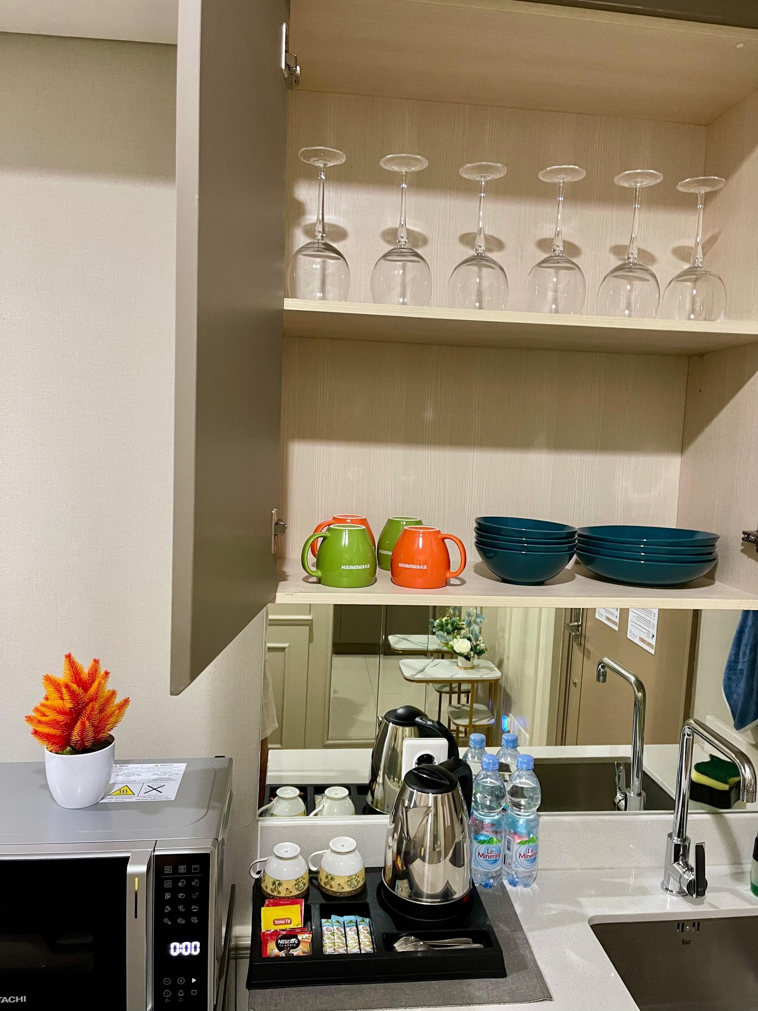A kitchenette with a microwave, coffee maker, tea set, and a sink.