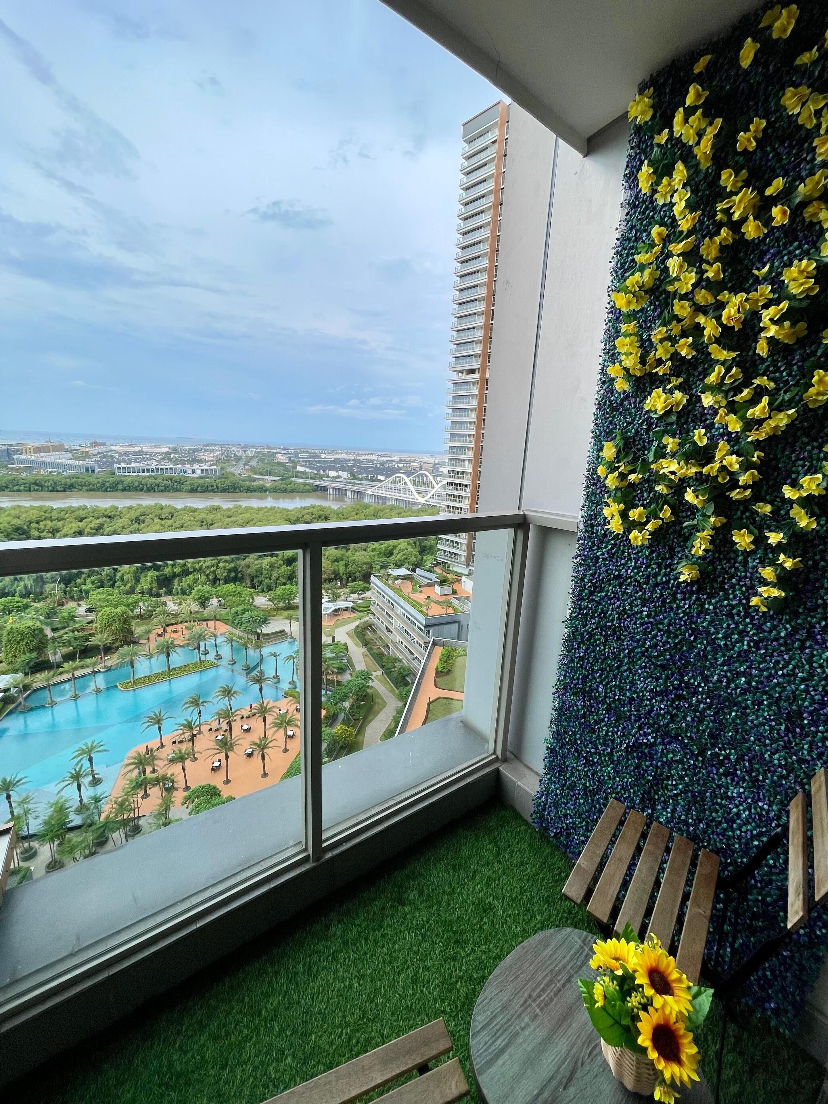 Un balcón con vistas a una piscina, una pared decorativa con flores amarillas y una pequeña mesa con un jarrón de girasoles.