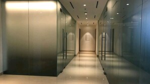 Un corridoio moderno e luminoso con pareti e porte in vetro, che conduce a un'area centrale con un quadro appeso al muro.