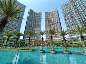 A modern hotel with a large pool area surrounded by palm trees and high-rise buildings. - Apartment Gold Coast PIK by MYsweethome (Jakarta)