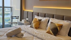 Una camera d'hotel moderna con un letto grande, vista sulla città tramite finestre a tutta parete e un balcone con sedia e tavolo.