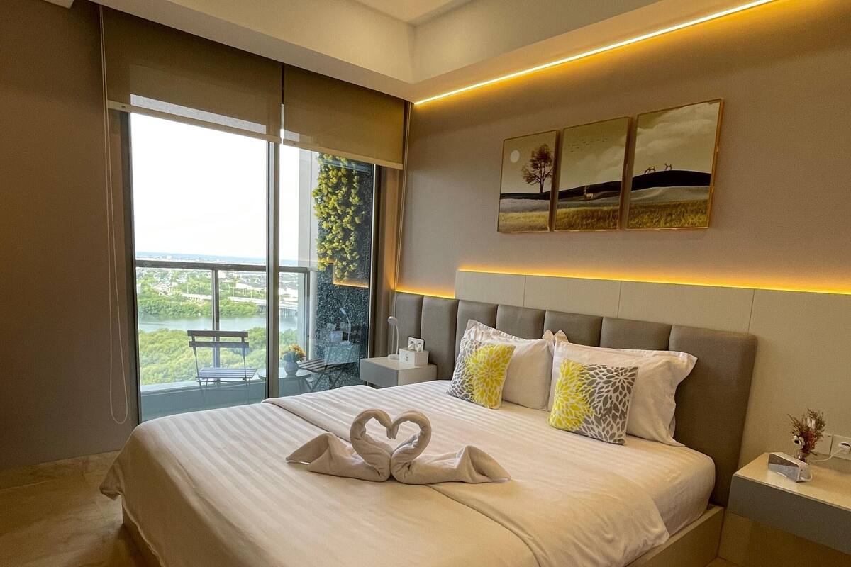 Un dormitorio moderno con una cama grande, vistas a un balcón y un paisaje urbano a través de la ventana.