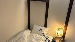 A neatly made bed with a white comforter and a decorative pillow. A small wooden nightstand with a lamp and a glass is beside the bed. - Pocket Seoul (Seoul)