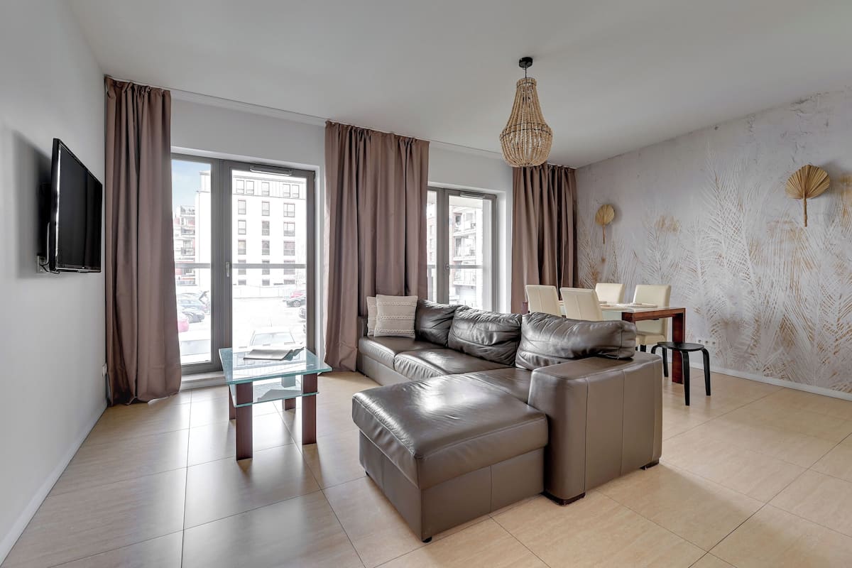 A modern living room with a sectional sofa, a glass coffee table, and a dining area with a table and chairs.