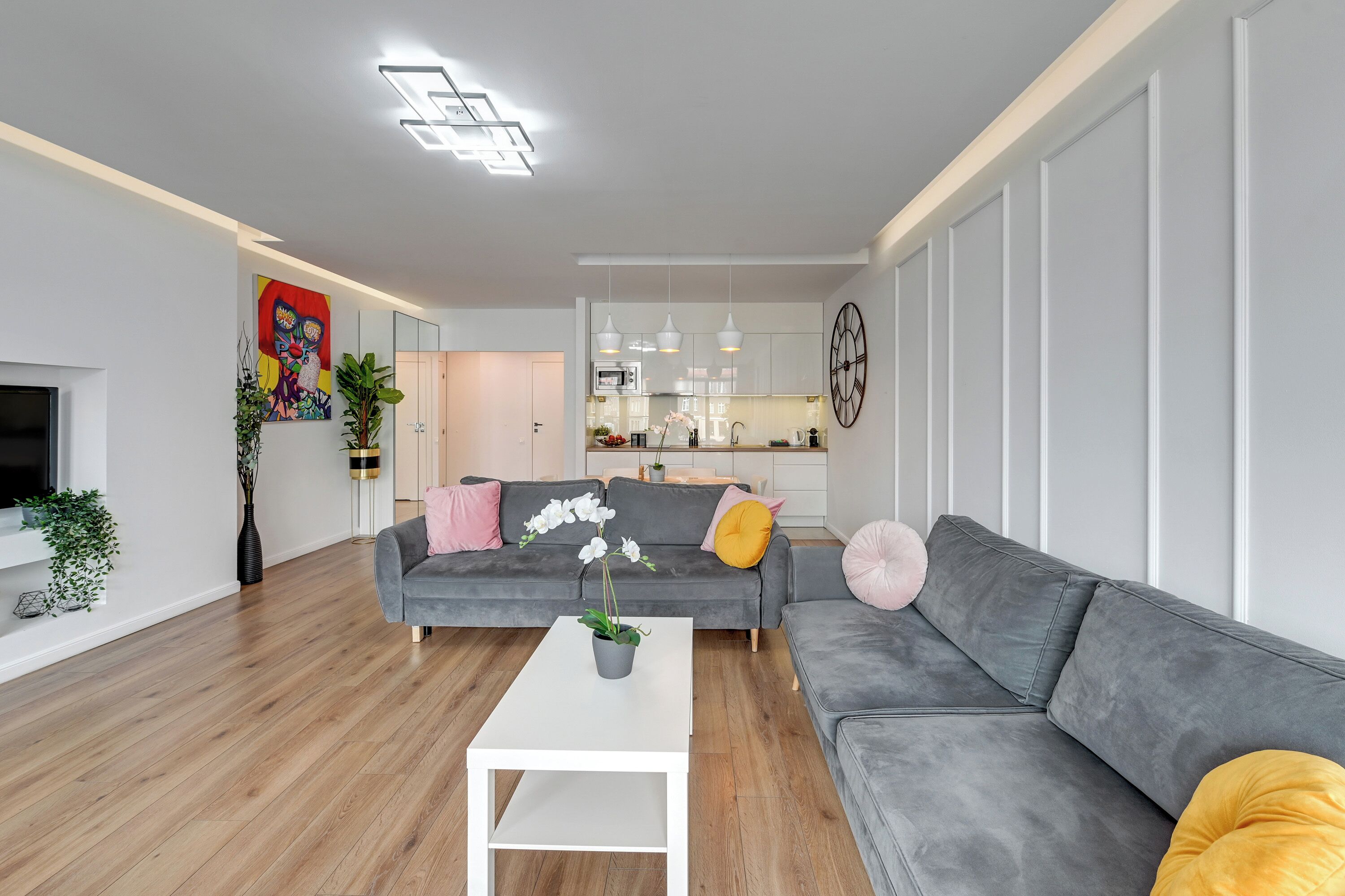 A modern living room with a grey sofa, a white coffee table, and a kitchen in the background.