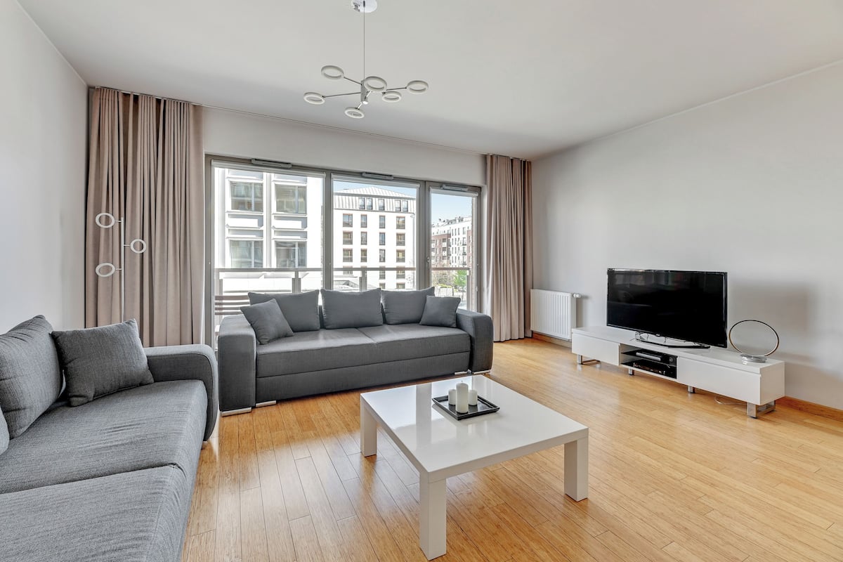 A modern living room with a grey sofa, a white coffee table, and a flat-screen TV on a white stand.