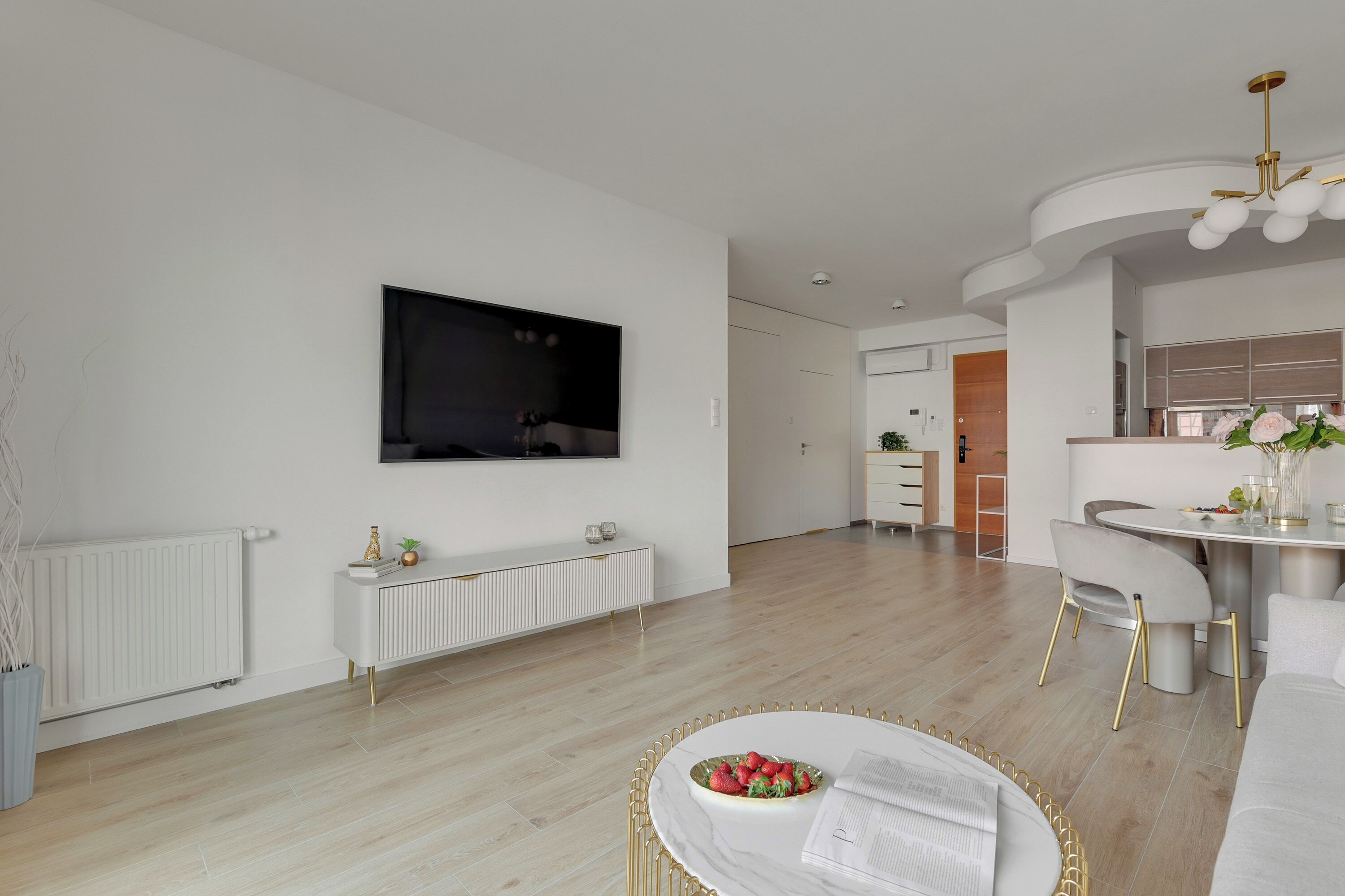 Ein modernes Wohnzimmer mit einem Flachbildfernseher, einer weißen Konsolentisch und einem runden Couchtisch mit Obstschale.