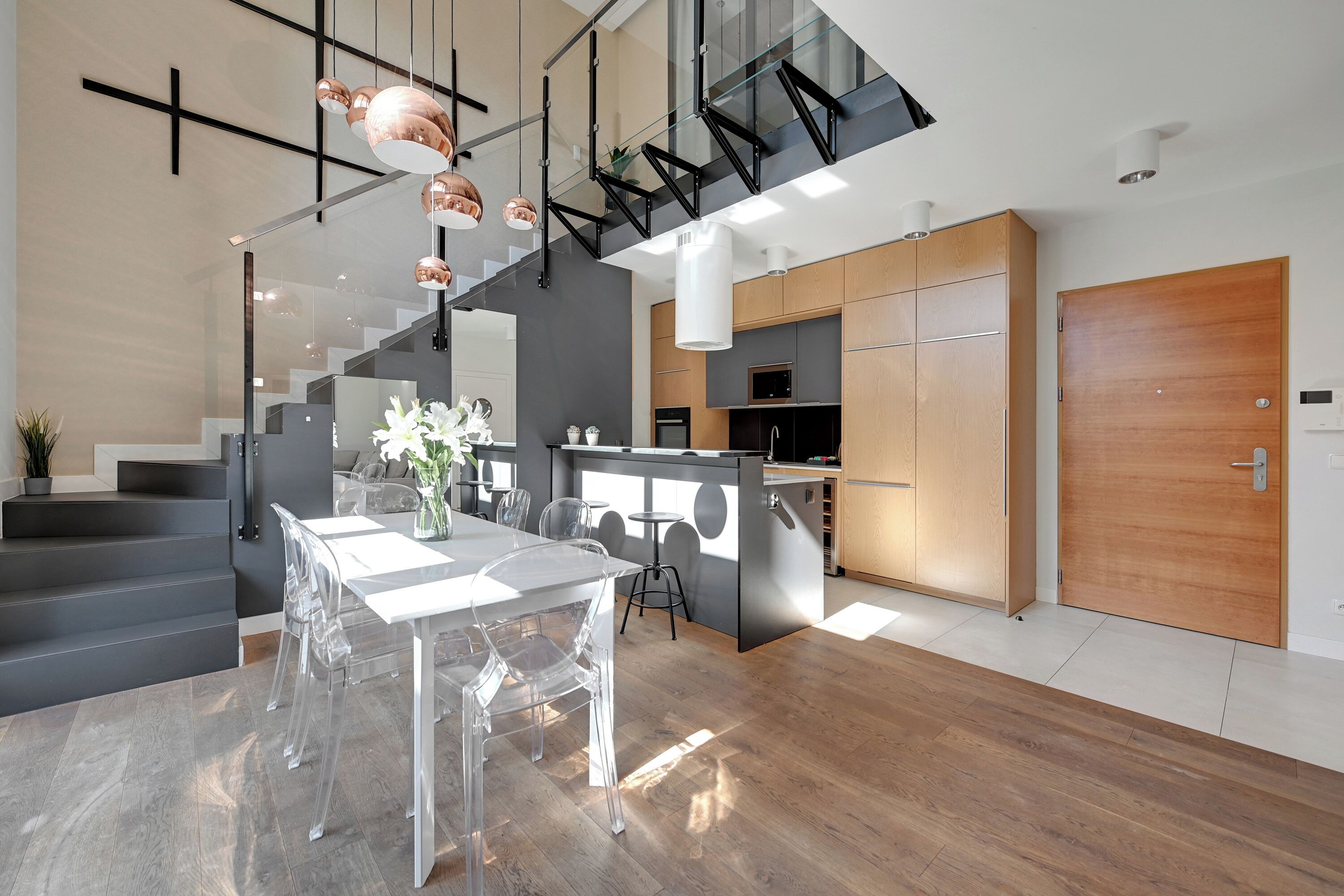 A modern kitchen with a central island, a dining area with clear chairs, and a staircase leading to an upper level.