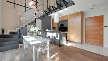 A modern kitchen with a central island, a dining area with clear chairs, and a staircase leading to an upper level.