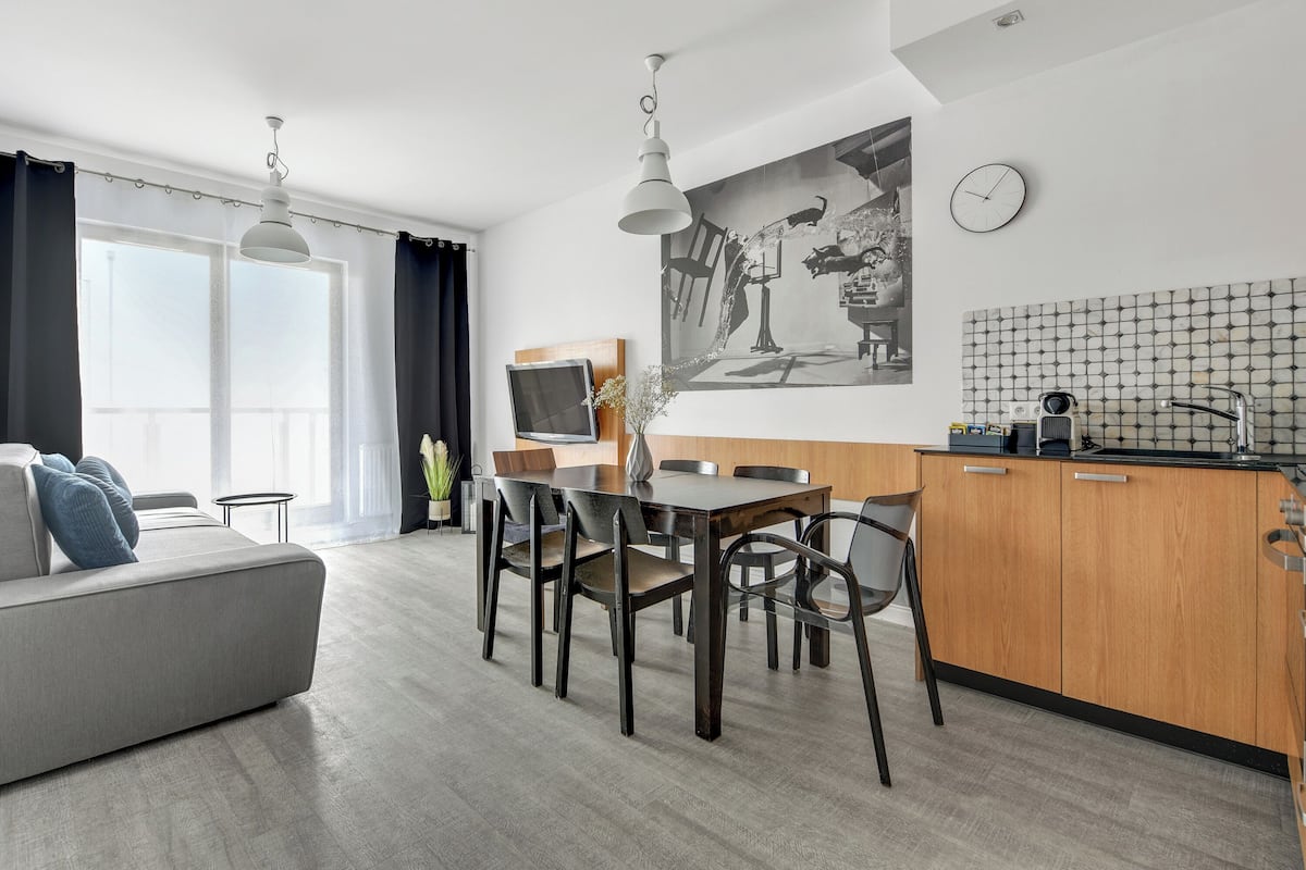 A modern living room with a sofa, dining table, chairs, and a kitchen area with a sink and countertop.