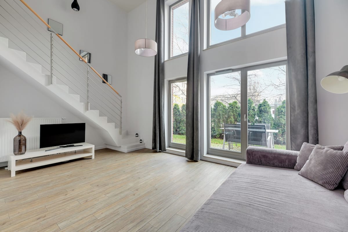 A modern living room with a staircase, large windows, and a sofa.