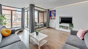 A modern living room with a grey sofa, a white coffee table, and a large window with curtains. - Waterlane Riverside - SPA, Pool, Gym & Parking by Downtown Apartments (Gdansk)