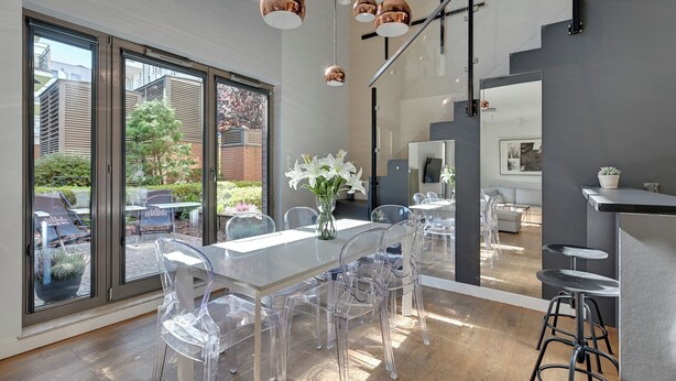 A modern dining area with a glass table and chairs, large windows, and a view of the outside. - Waterlane Riverside - SPA, Pool, Gym & Parking by Downtown Apartments (Gdansk)