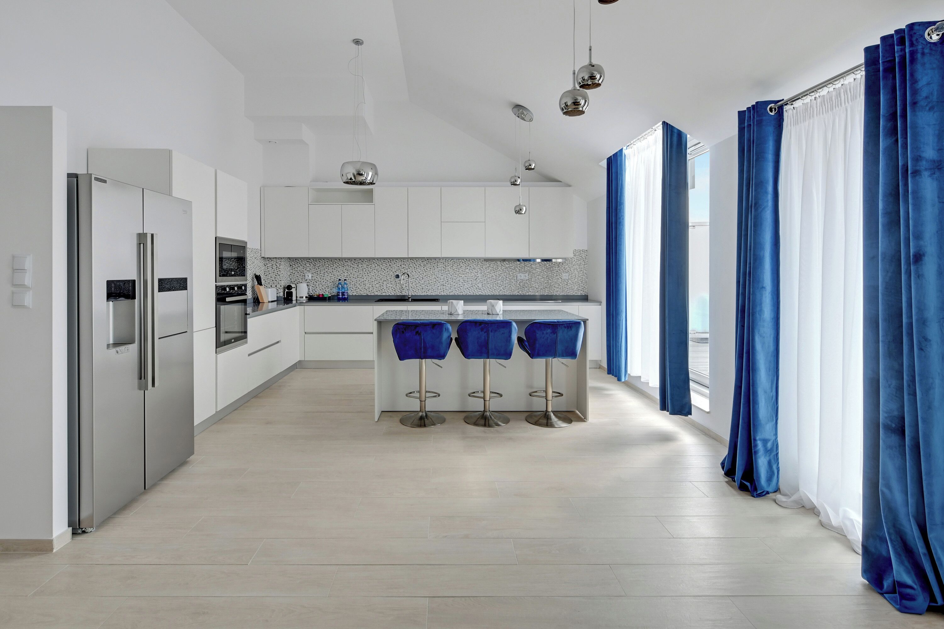 A modern kitchen with stainless steel appliances, a central island with bar stools, and a view of the city through large windows.