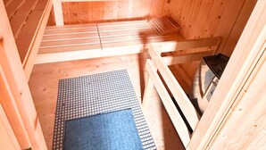 A sauna room with wooden benches, a mat, and a heating element. - Berghupferl-Alm (Flintsbach A. Inn)